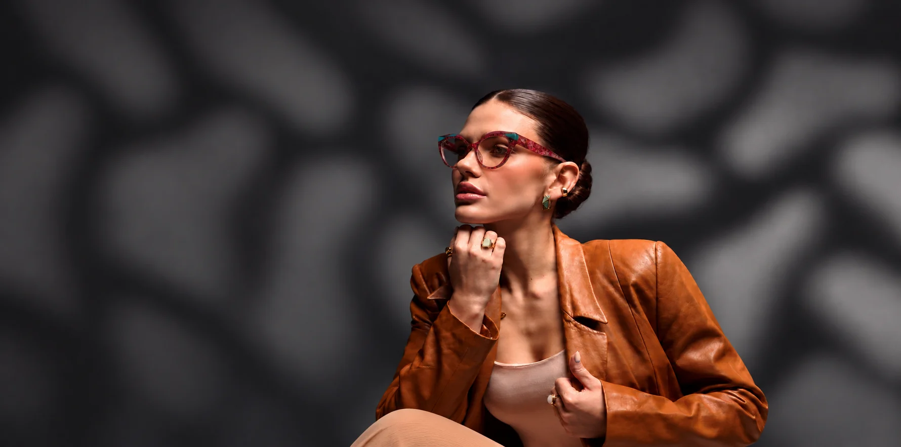 Model in a tan leather jacket wearing pink and turquoise cat-eye glasses